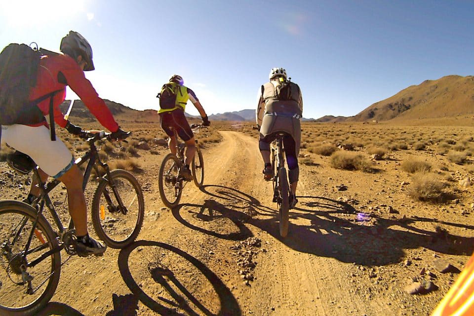 3 people ride mountain bikes through desert