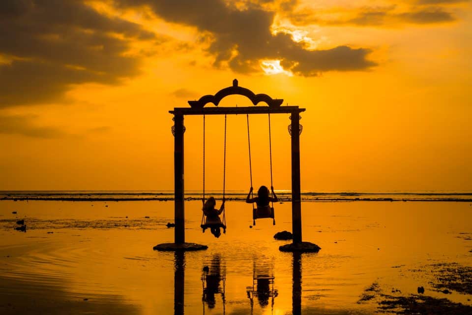 Two girls swing at sunset on Gili Islands, Indonesia