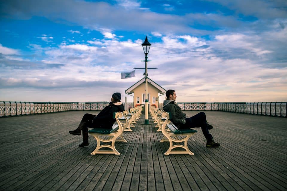 A couple sitting back to back on a pier