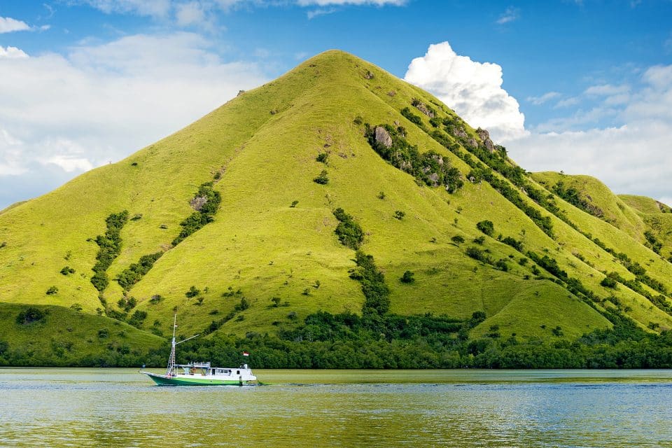 A boat sailing past a green mountain