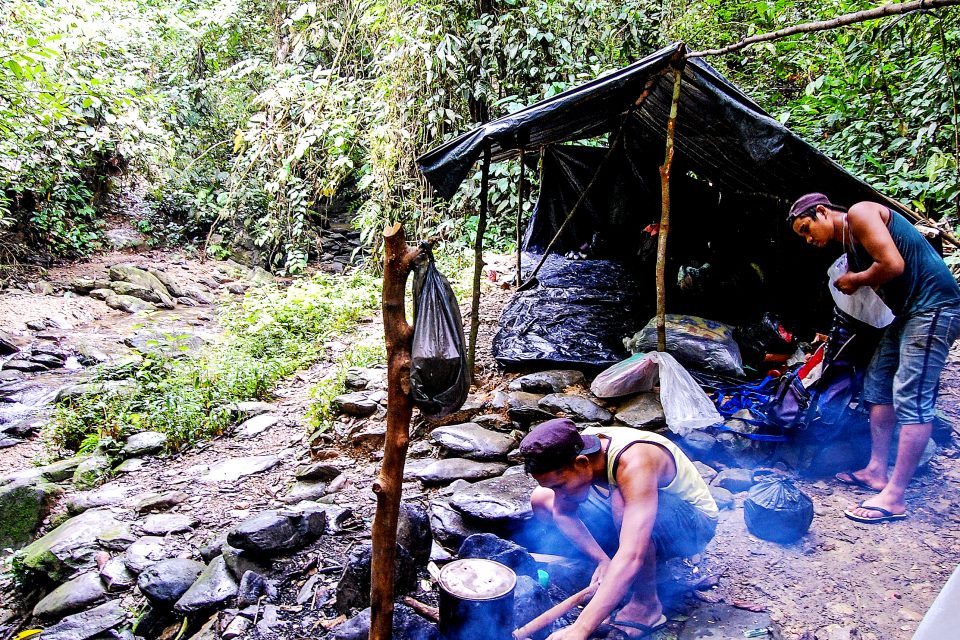 Two men cooking food next to their shelter
