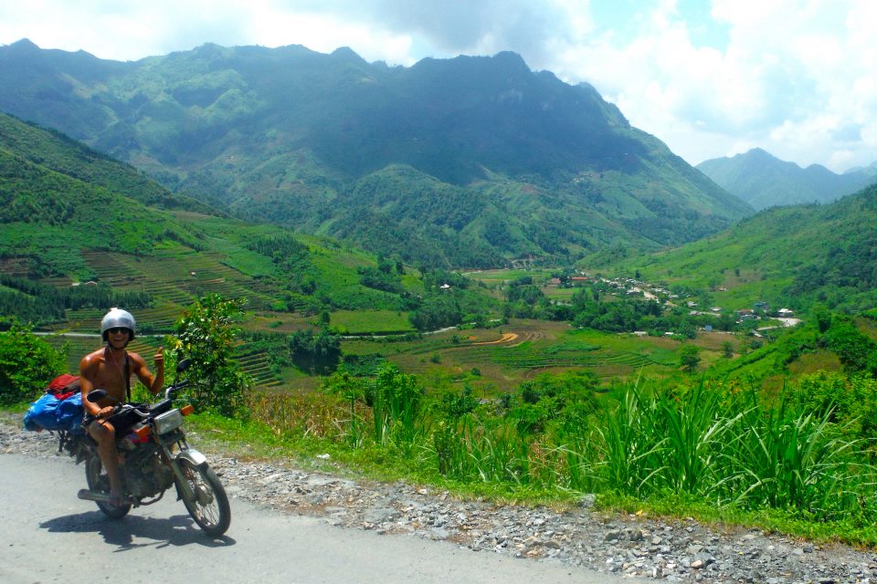 A man sat on a motorbike in front of mountains
