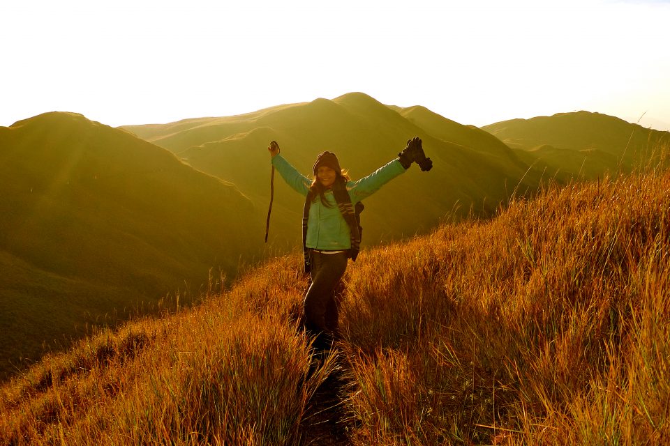 A woman with her arms outstretched with mountain peaks behind