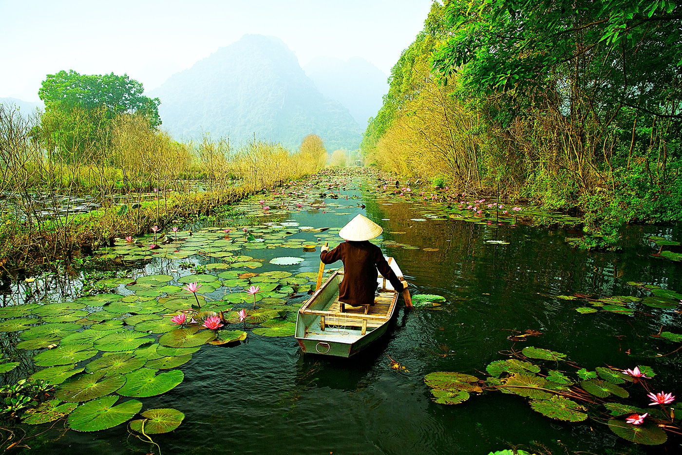 A woman paddling down a river full of lily pads on a canoe
