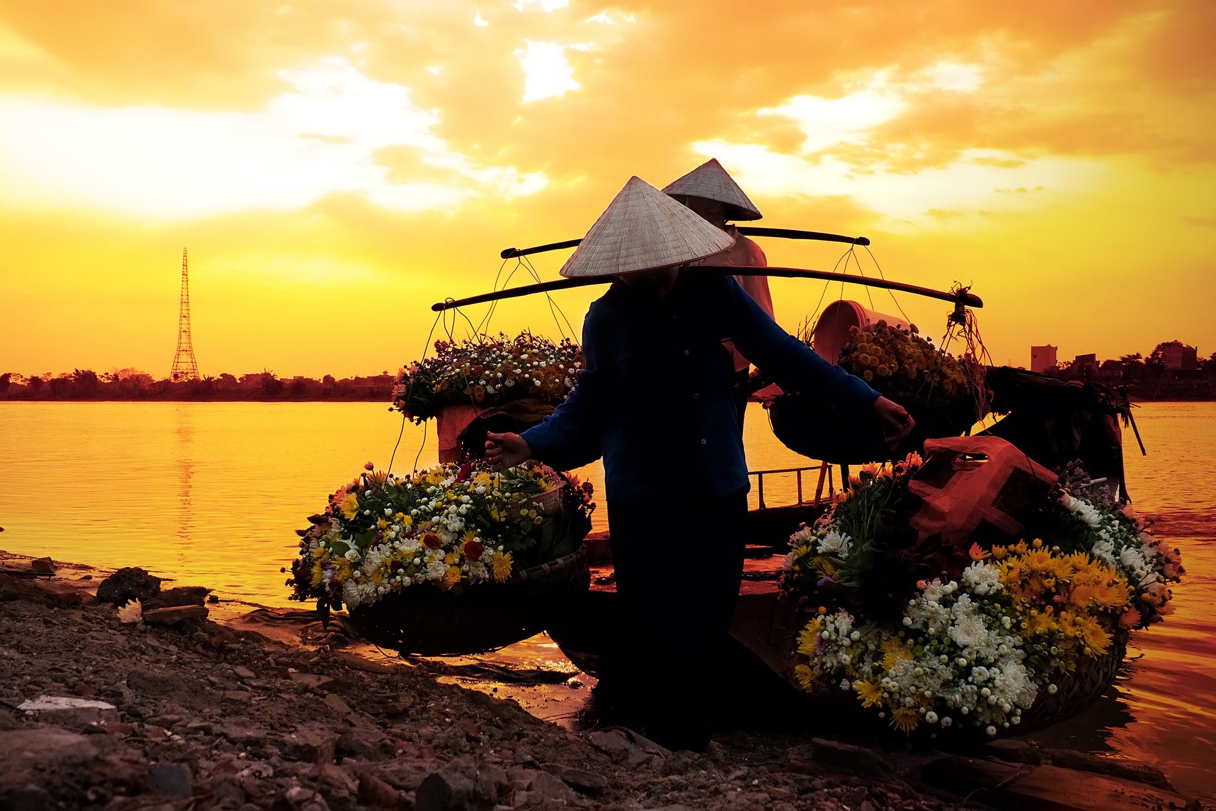 Two women carrying flowers off canoes at sunset
