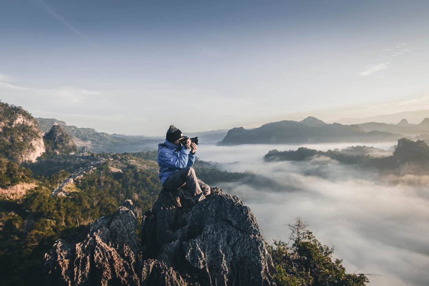 person taking photo sitting on rock in the mountains
