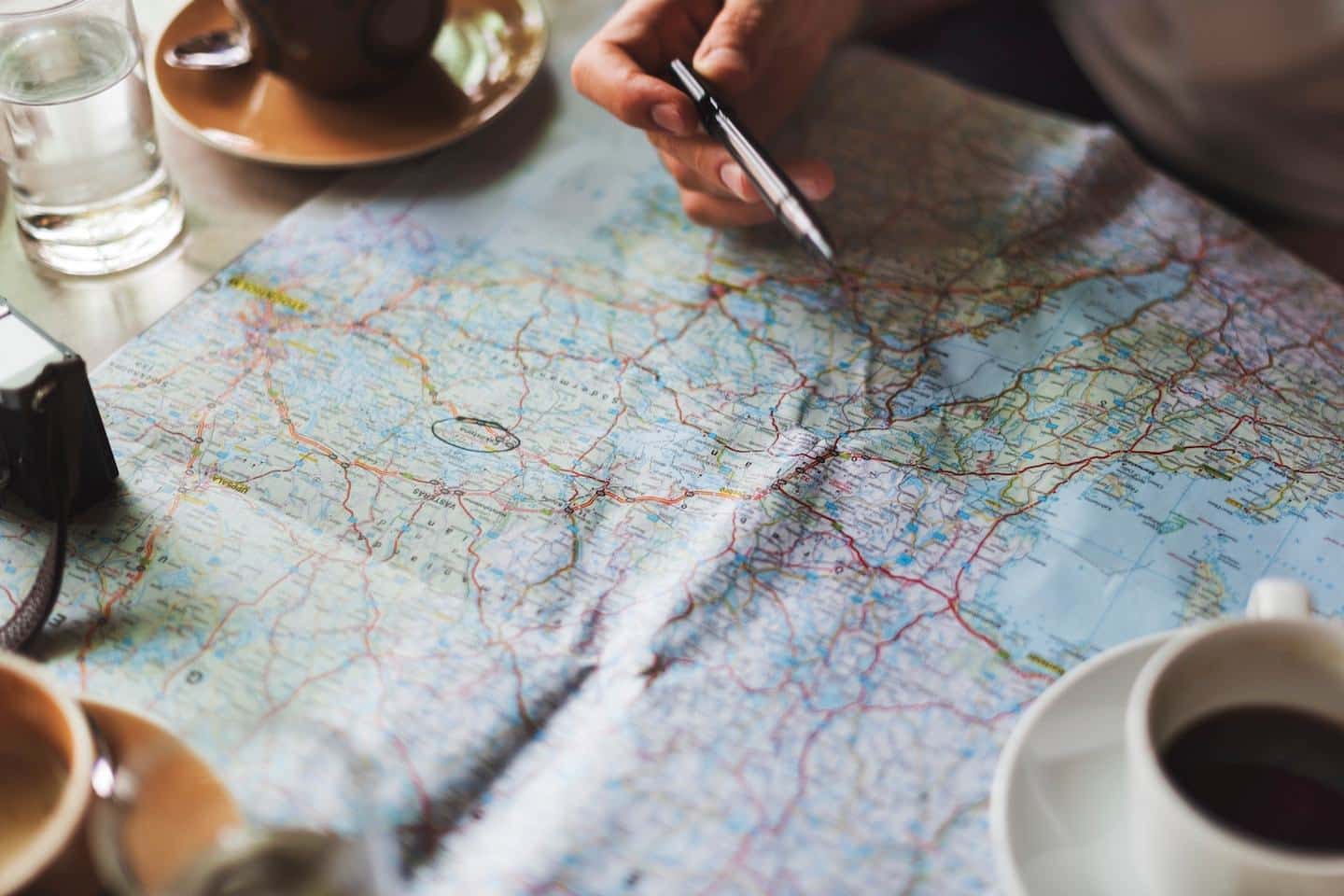 a person holding a pen over a map with coffee