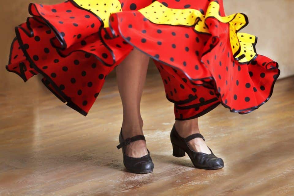 view of a woman's feet and bottom of her red and yellow dress as she dances flamenco