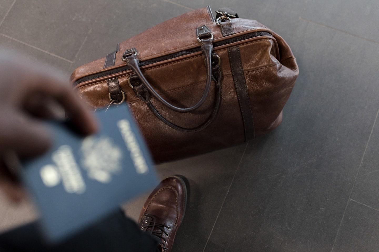 person with leather duffel bag and passport
