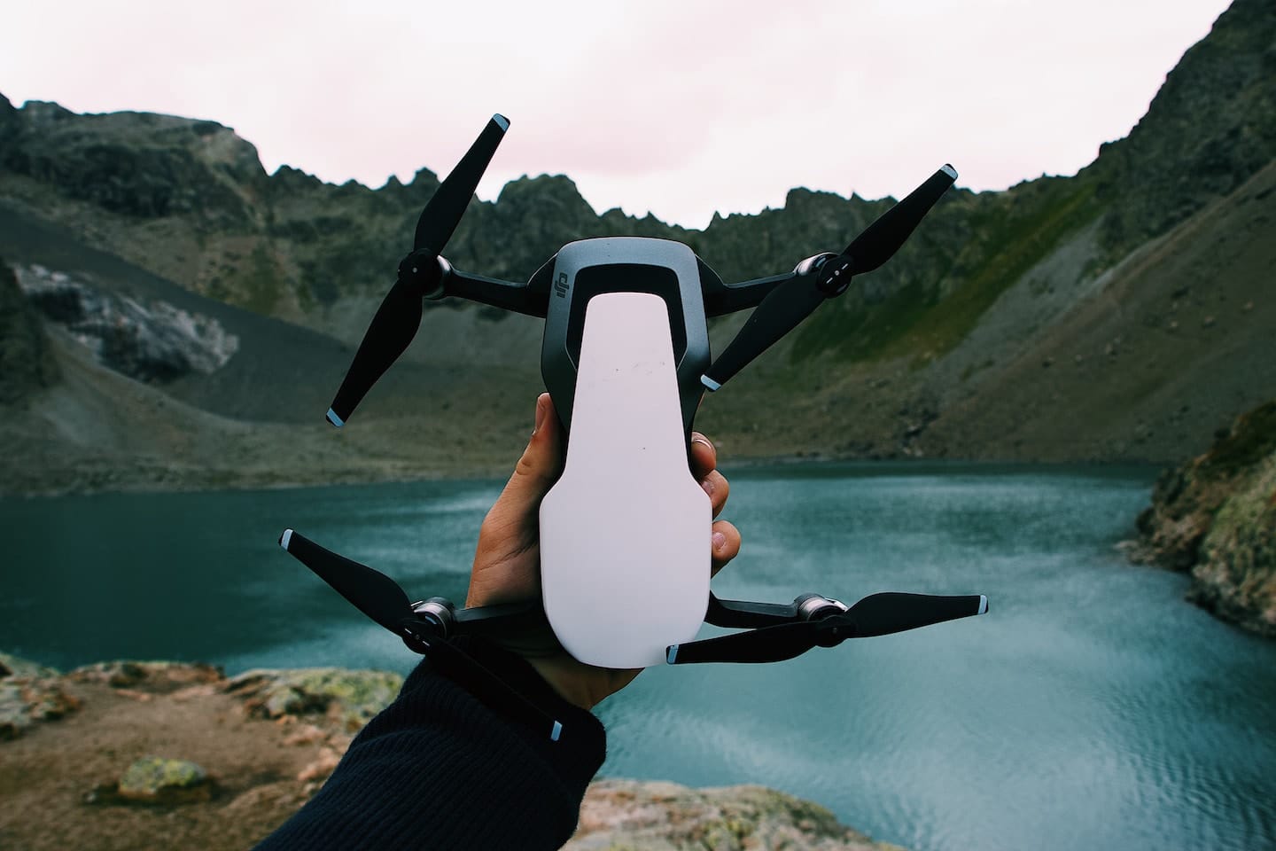 person holding drone in front of water and mountains