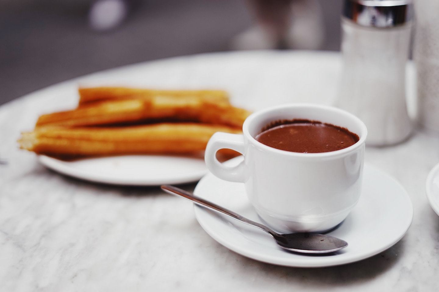 cup of chocolate with churros in the background