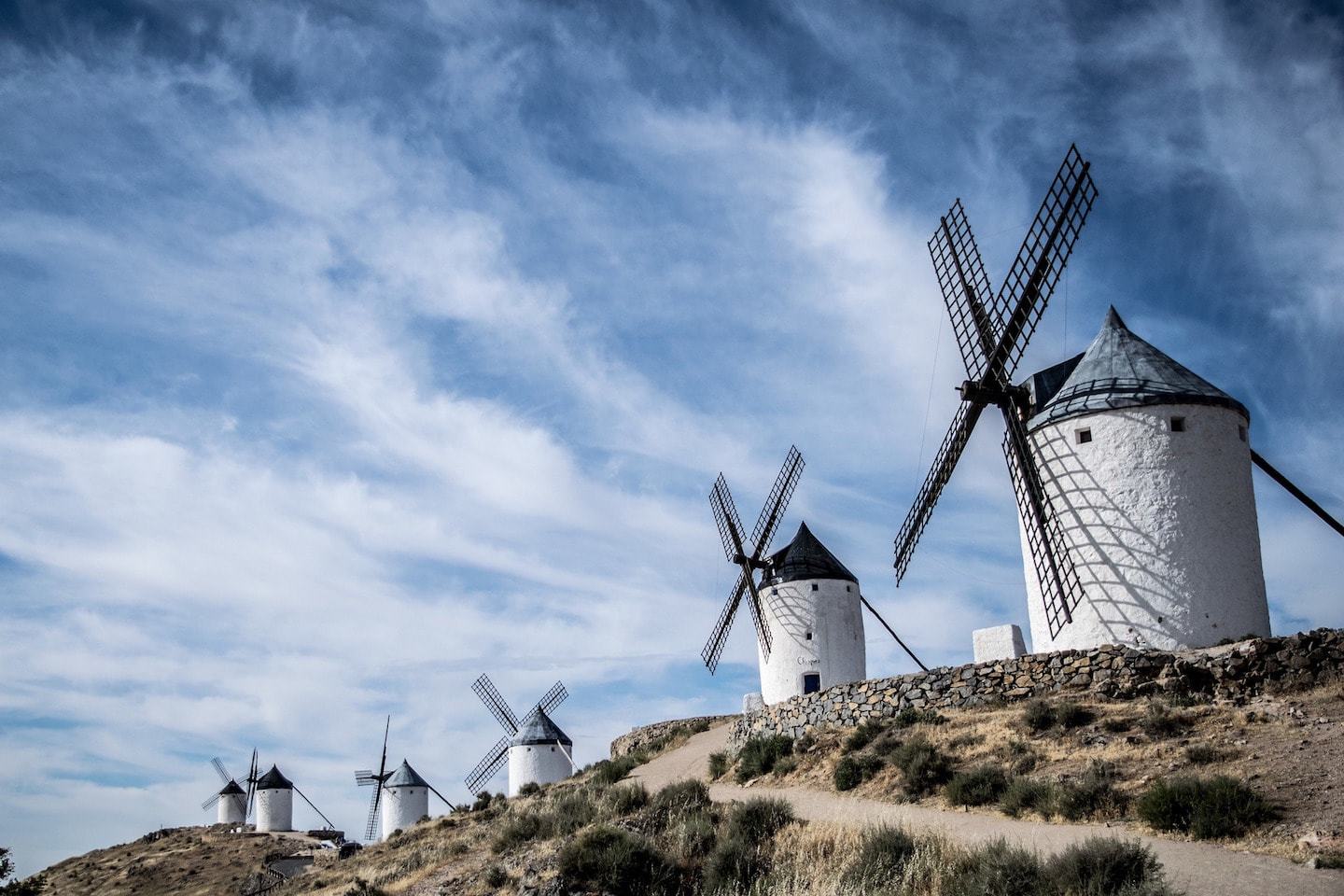 large white windmills against a blue sky in consuegra spain