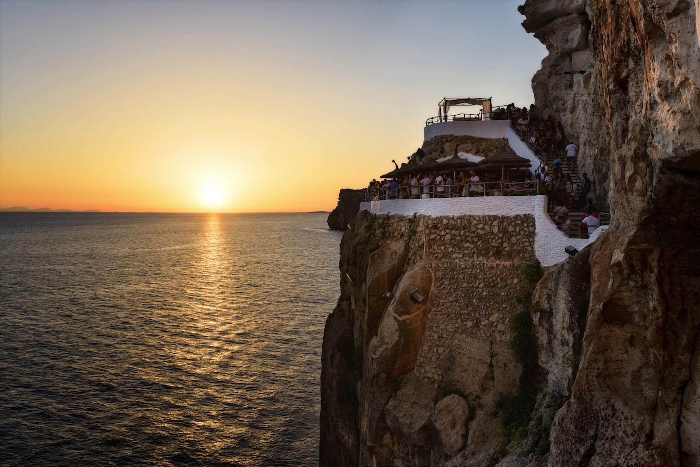 bar on the side of a cliff overlooking the water during sunset