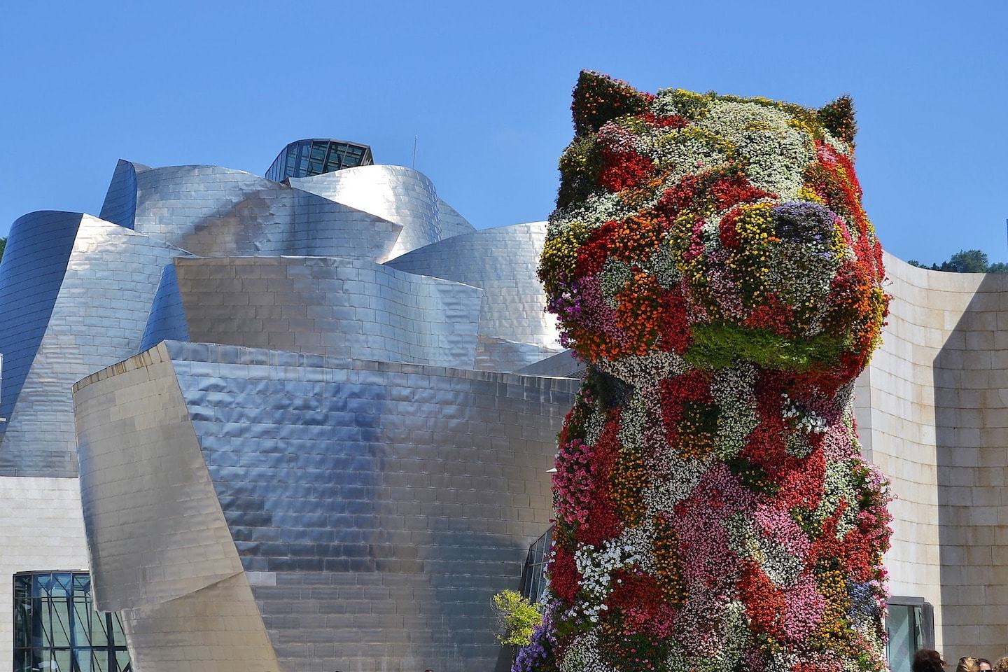 big sculpture of dog with flowers on it with modern metal building behind