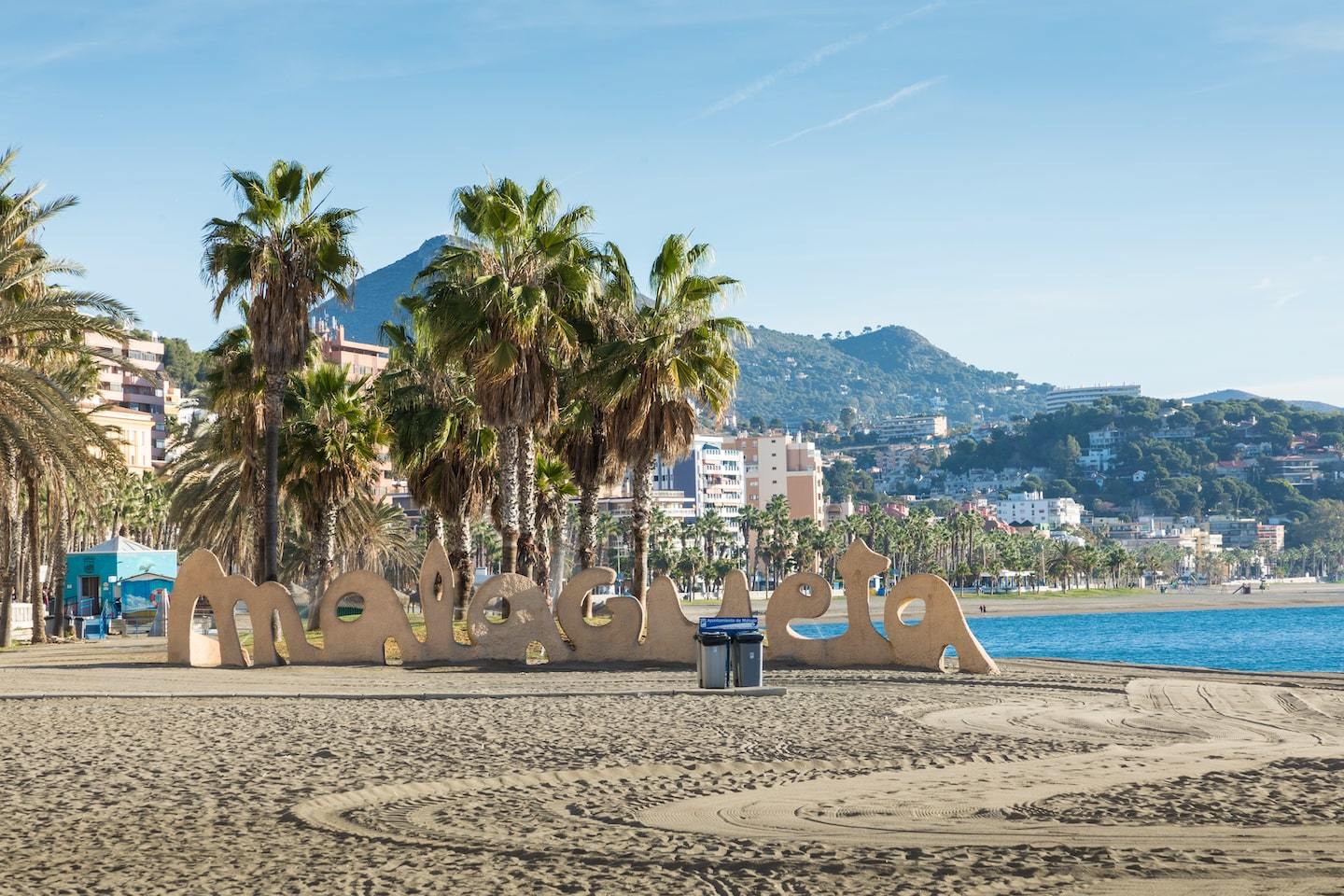 beach with large sign reading malagueta with palm trees and mountains behind