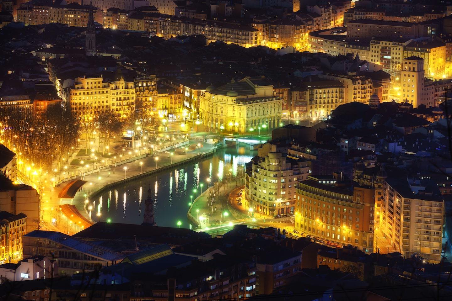 Aerial view of Bilbao at night with buildings lit up around the river