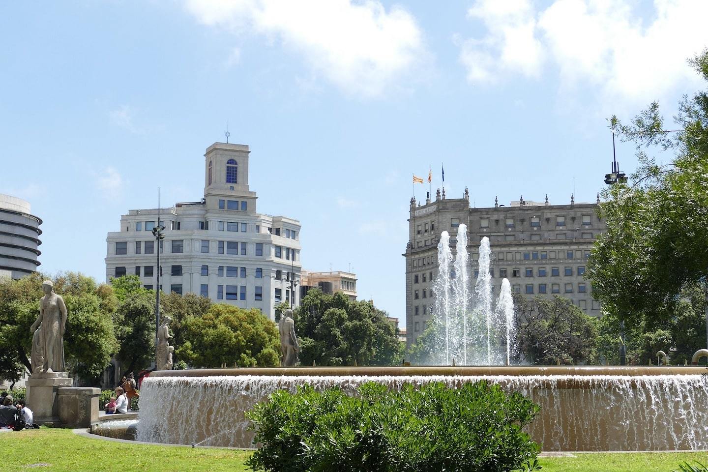 fountain surrounded by grass, trees and buildings