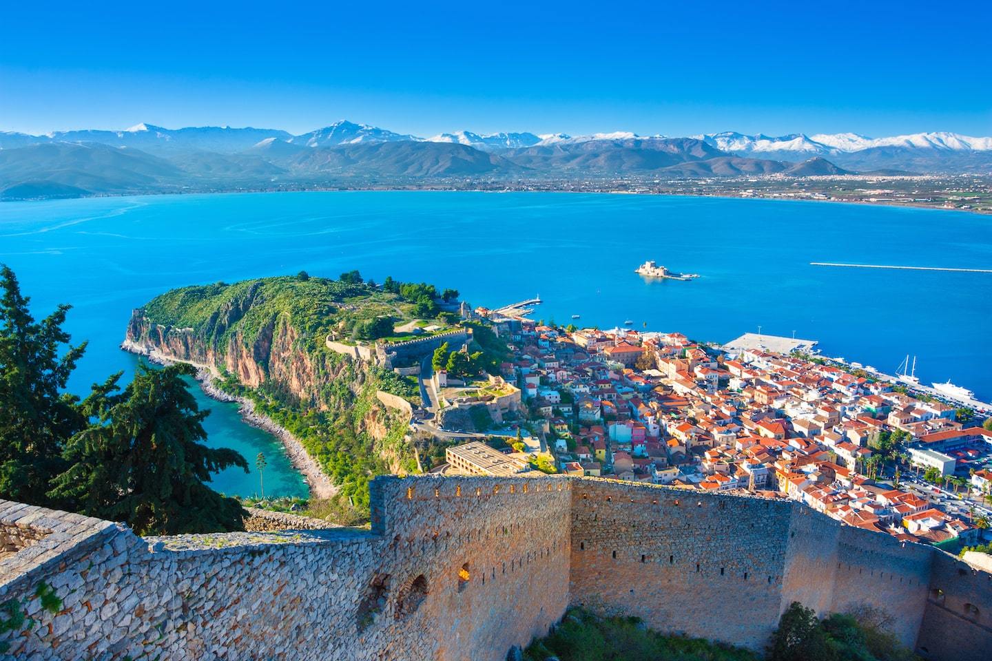 Aerial view of Nafplio, Greece with a piece of land jutting out into the water with mountains behind.