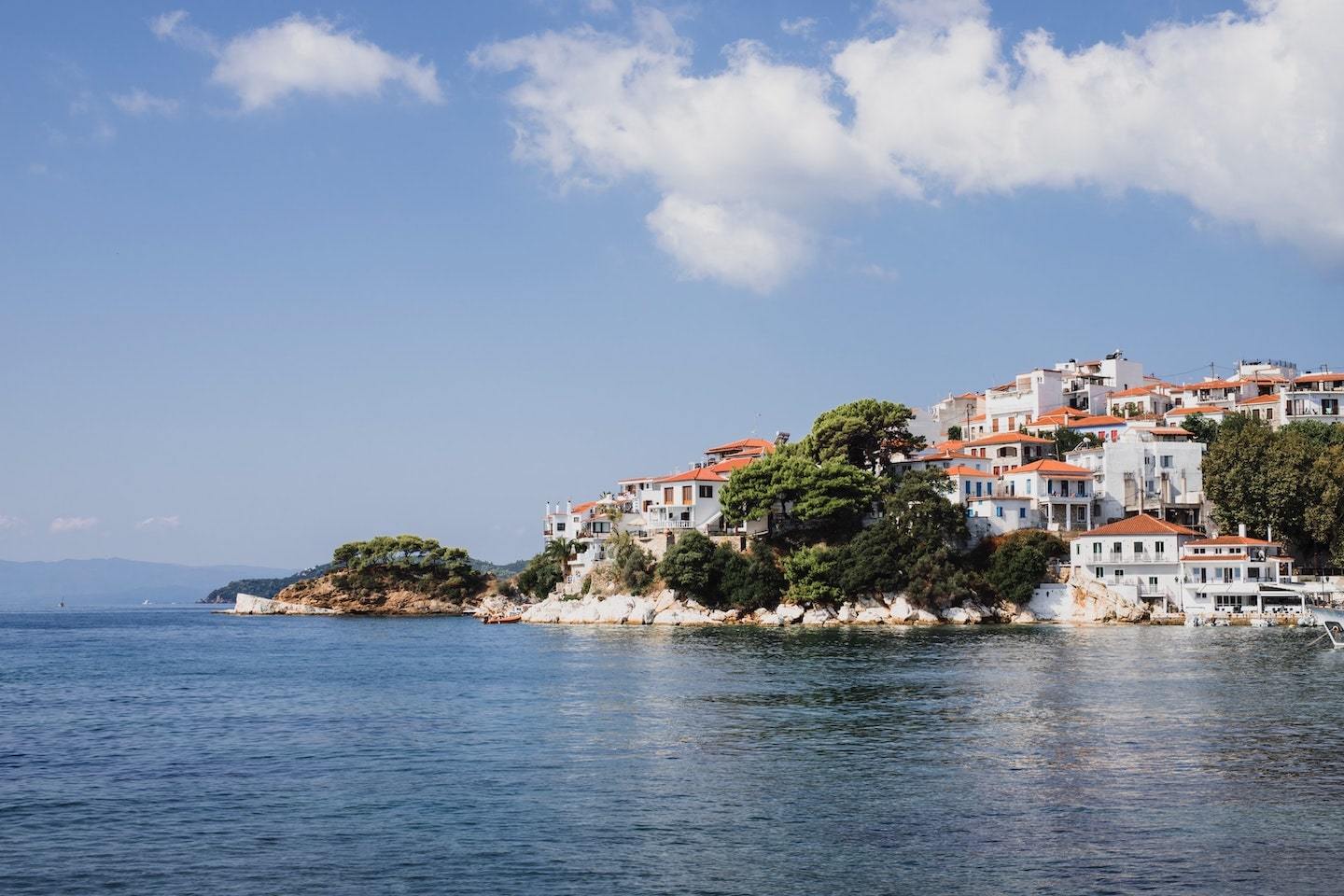 Houses sitting on a hill in front of the ocean in Skiathos, Greece