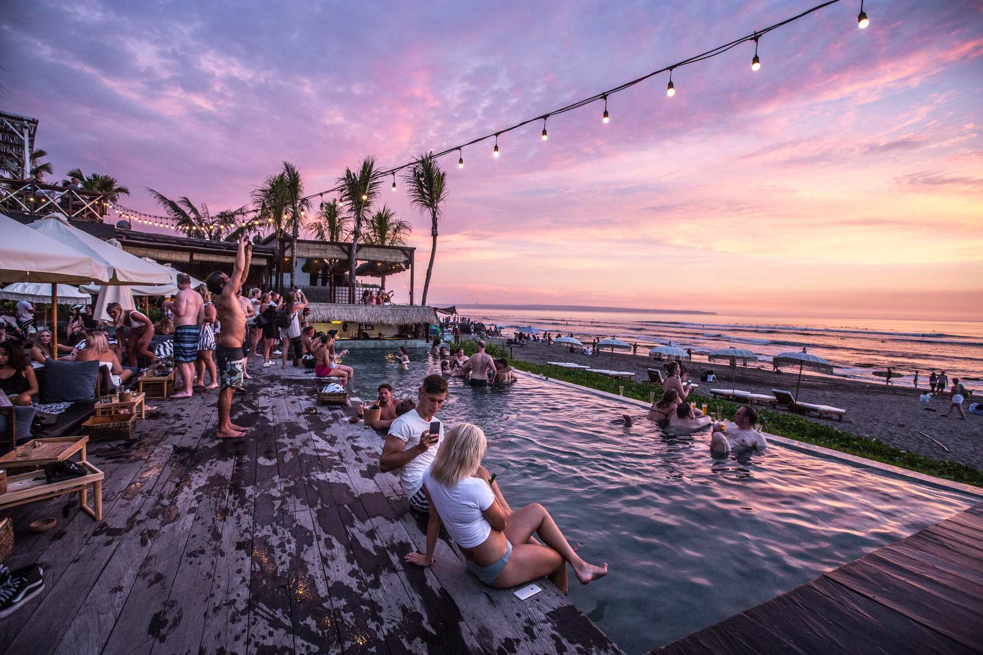 people in and around a pool on a beach at sunset in bali