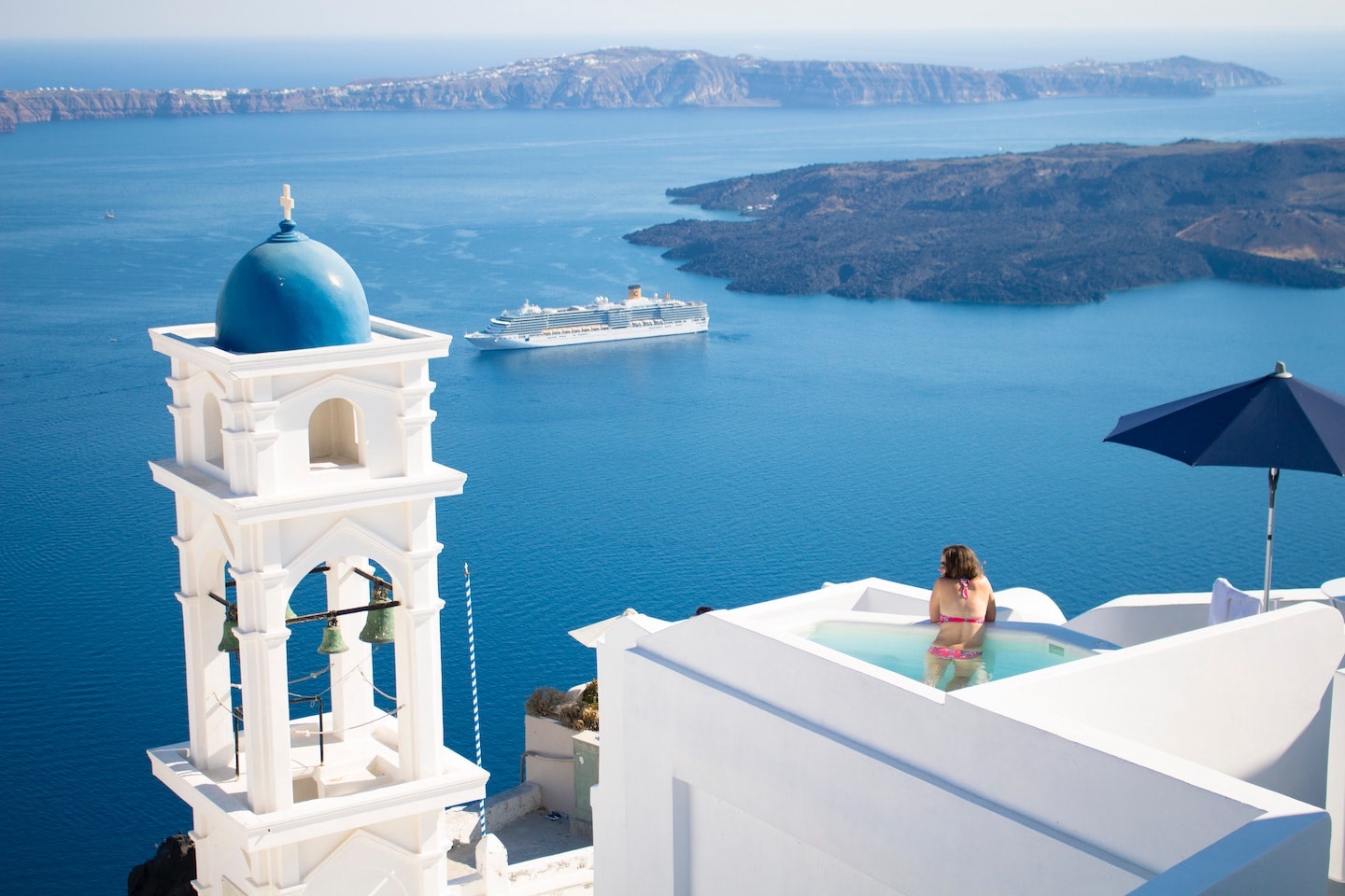 person in a pool overlooking the sea and islands in Santorini Greece