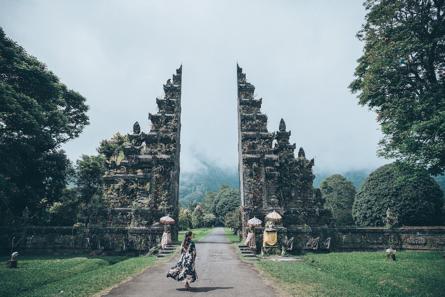 person walking towards large bali gate surrounded by greenery on a misty day
