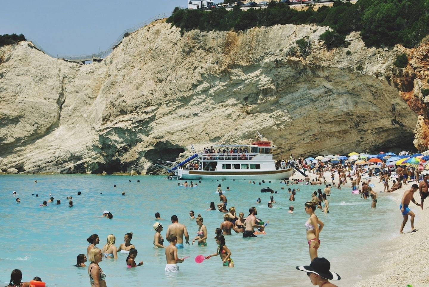 Lots of tourists on a beach surrounded by a huge rock in Greece