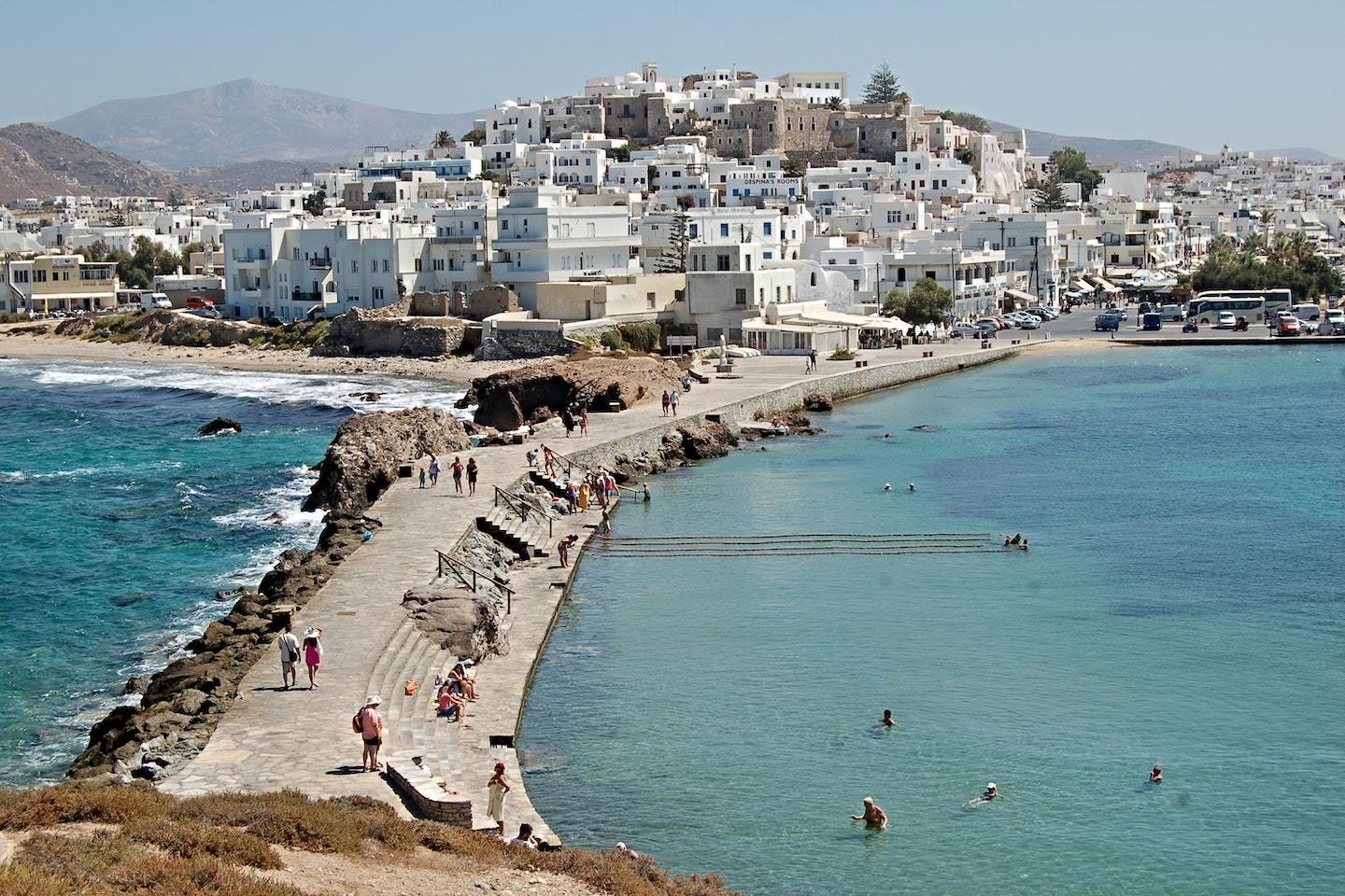 Naxos town with white houses on top of a hill connected to the sea by a thin strip of land.