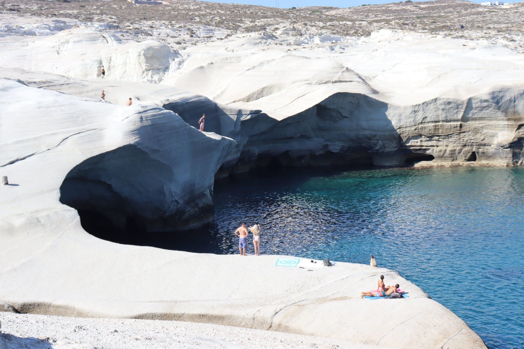 Smooth white rocks with people standing on them surrounded by water in Milos Greece