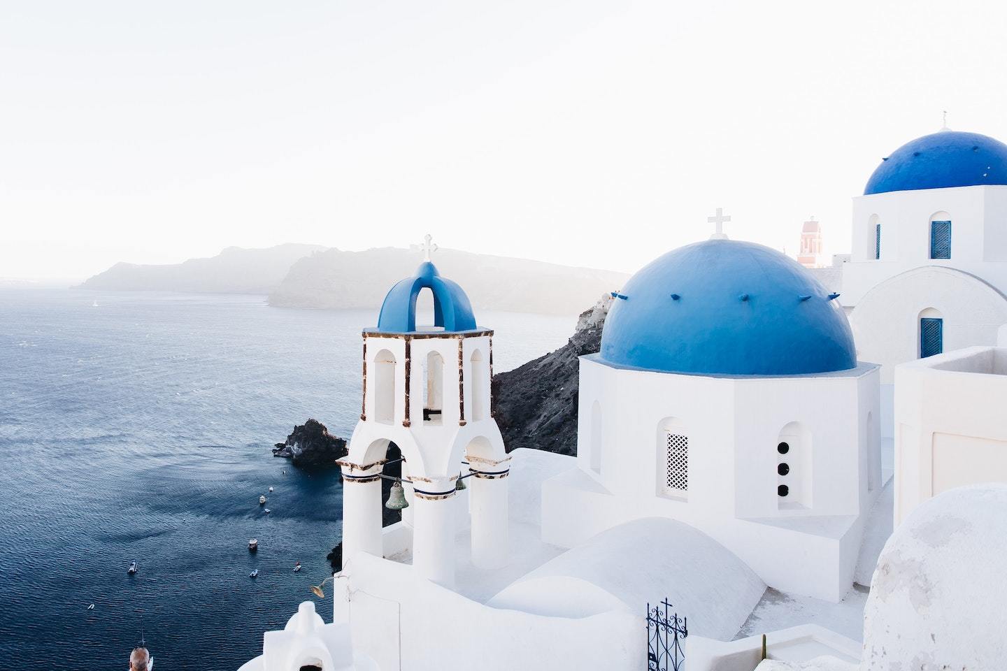 Best Greek islands to visit: blue and white domed church with ocean behind in Santorini Greece