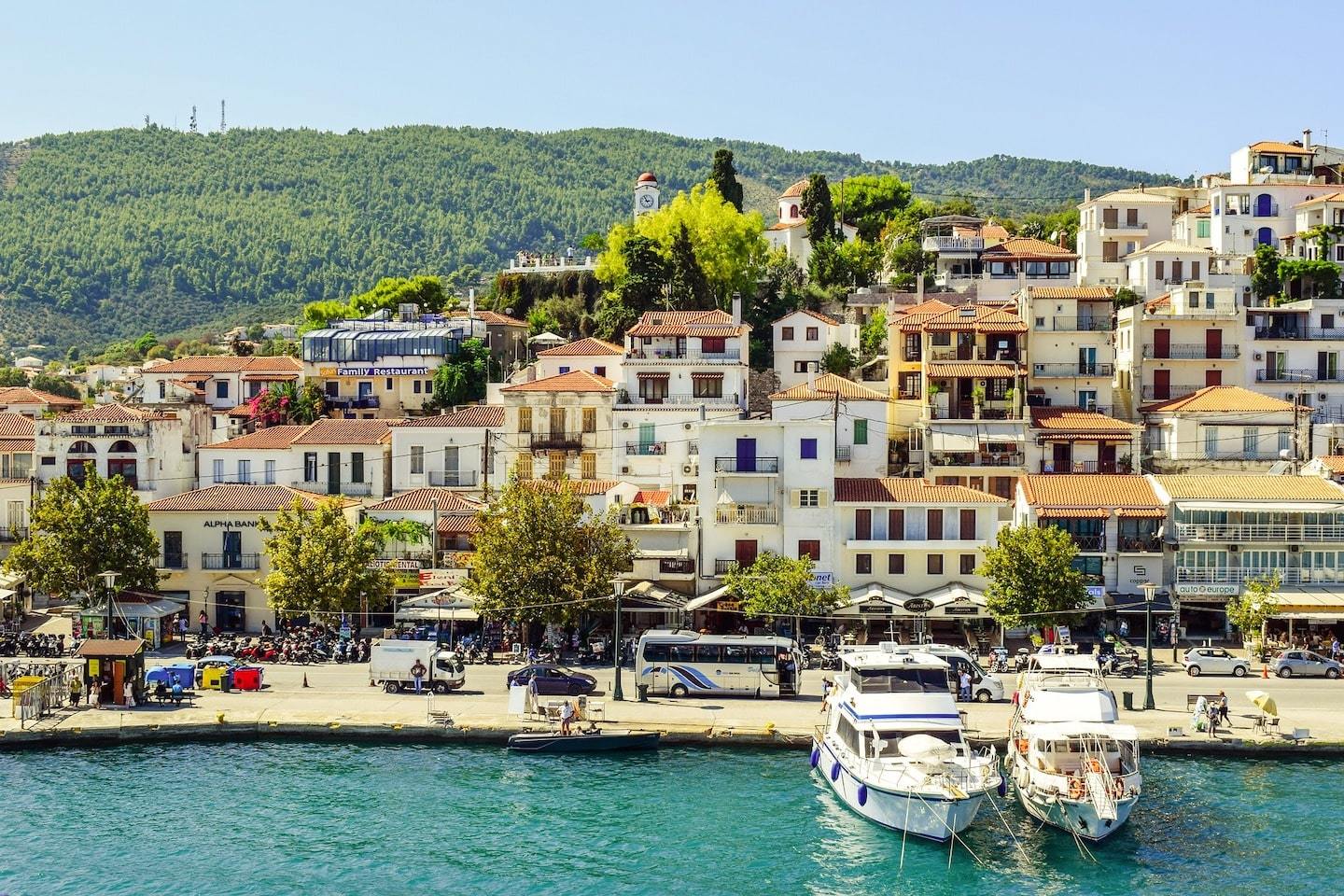 colorful buildings with hill behind and sea with boats in front in Skiathos Greece