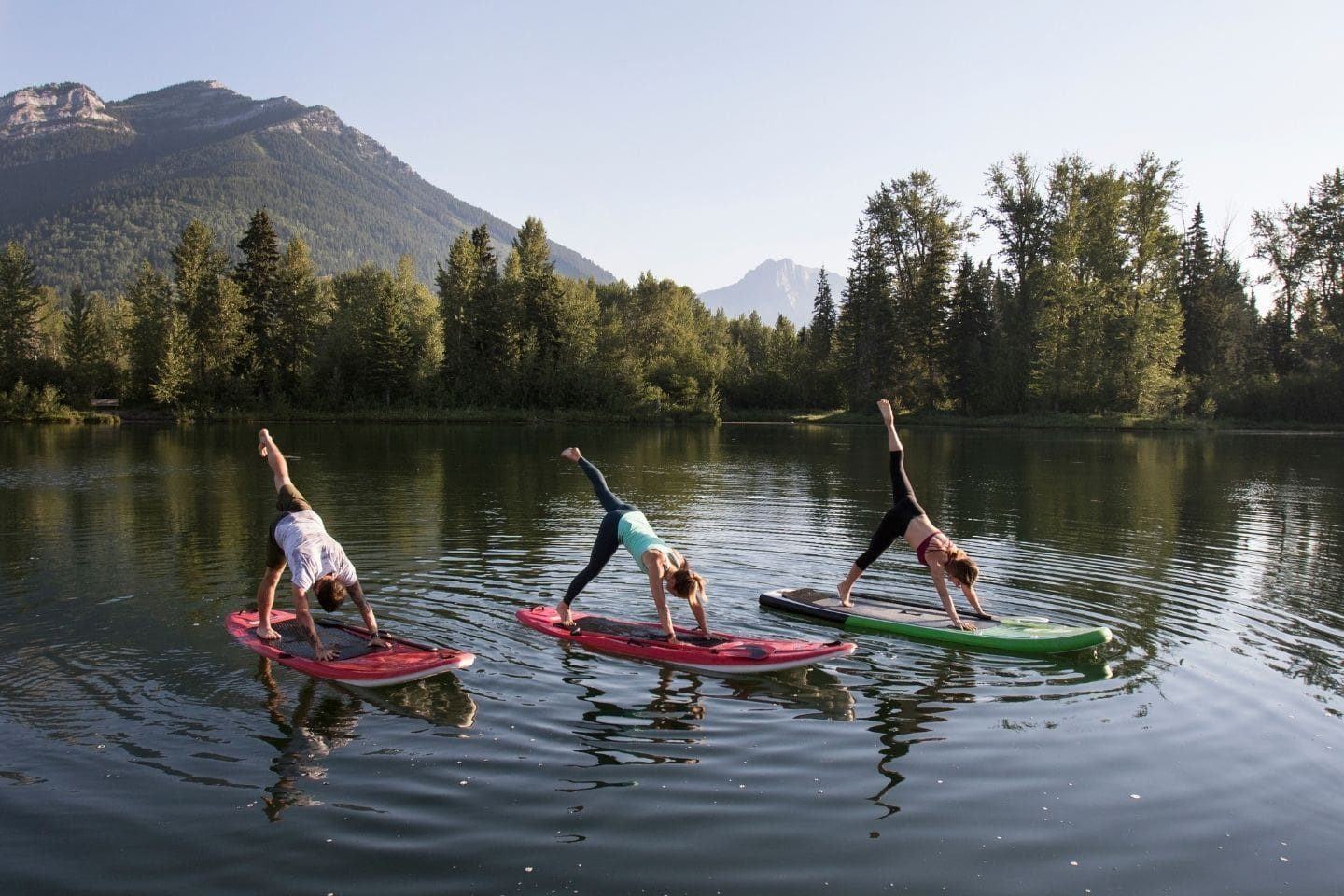 Three people practicing yoga on paddle board with mountains on the background