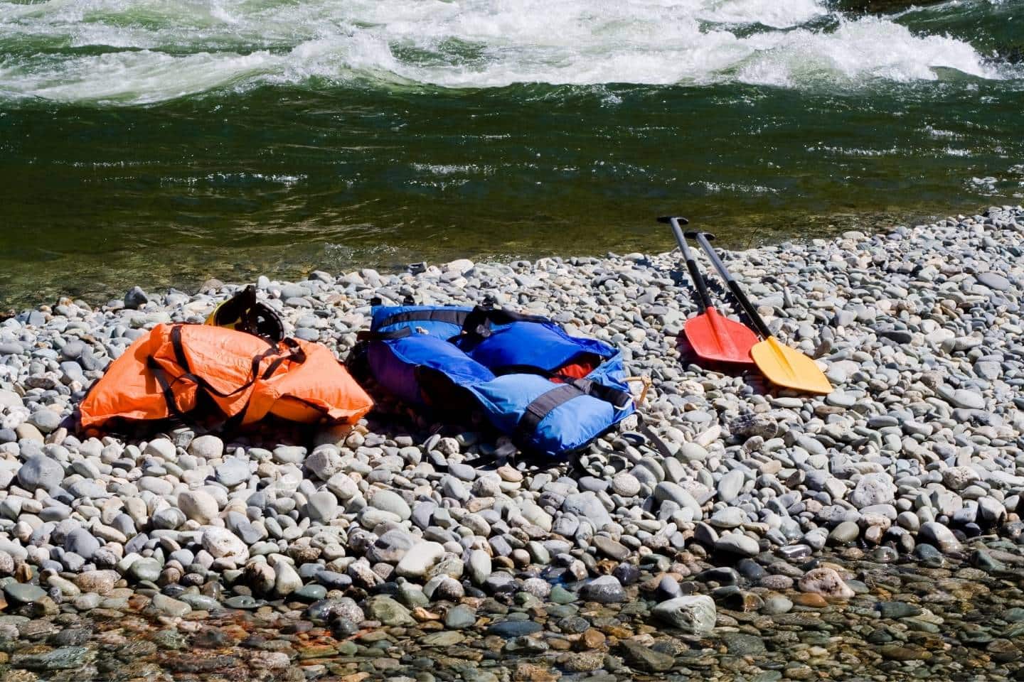 Two life jackets and two paddles on stones near the stream