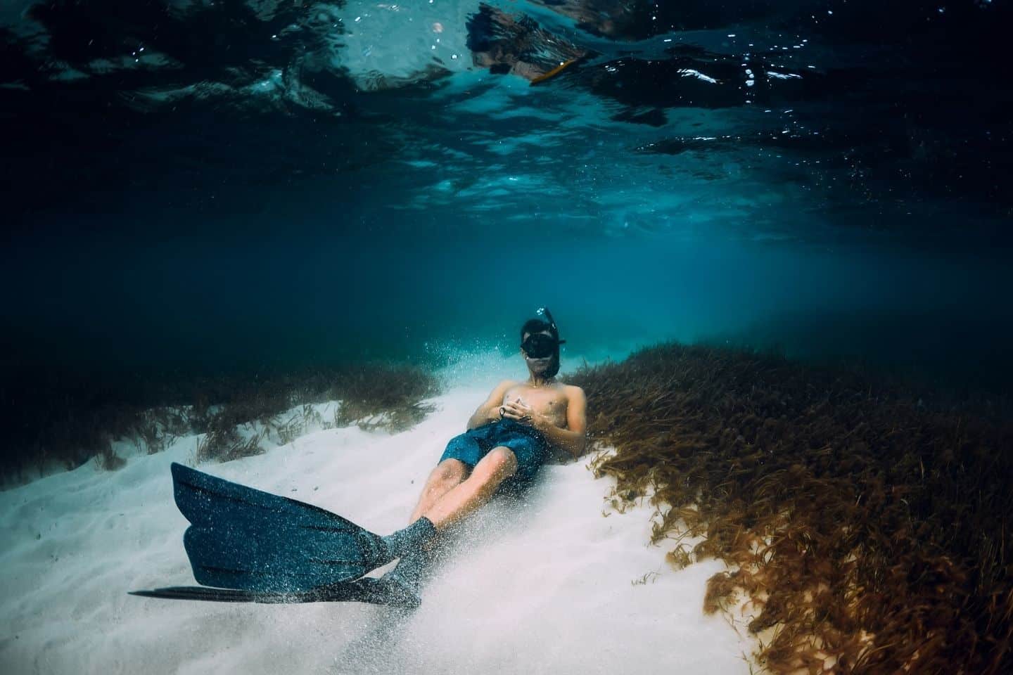 Freediver man with freediving fins relax over sandy bottom in blue ocean