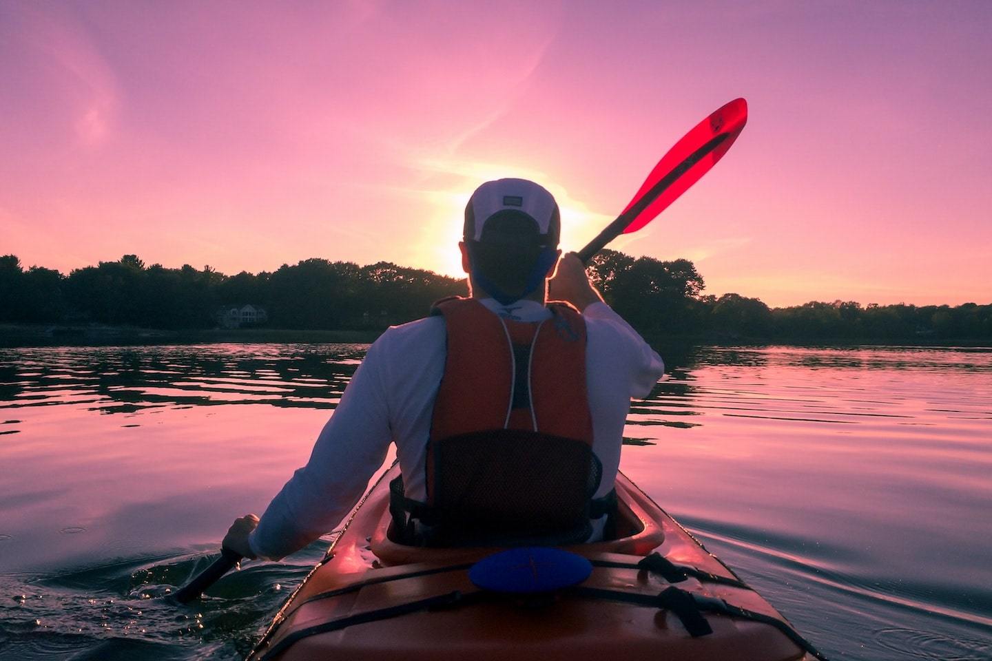 man kayaking wearing a pdf at sunset