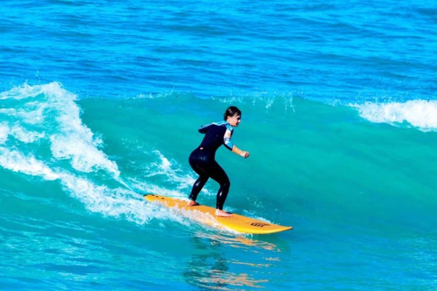 A surfer on top of a surfboard riding a wave in the beach