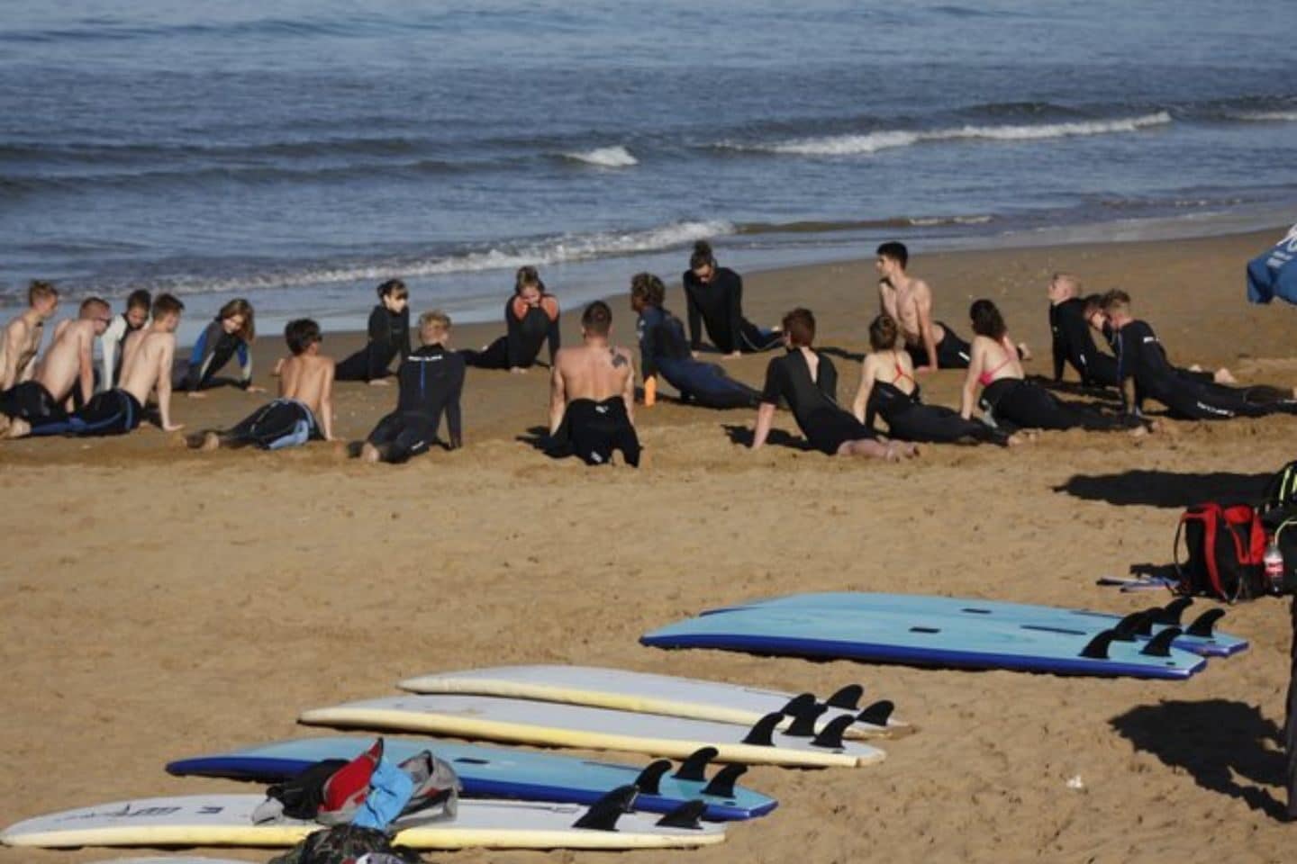 Group of surfers in black wet suits on the beach sand